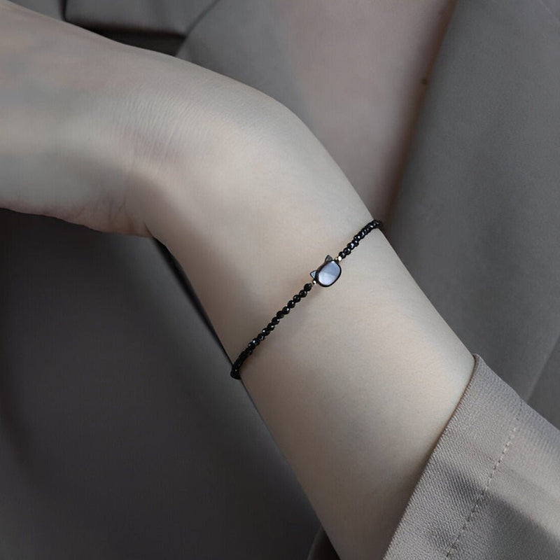 Bracelet fin en pierres noires avec pendentif tête de chat en cristal blanc sur poignet féminin.