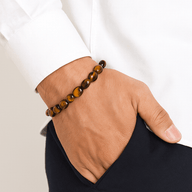 Bracelet en œil de tigre avec perles rondes lisses sur poignet, style asymétrique, ton marron brillant.