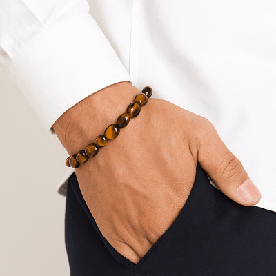 Bracelet en œil de tigre avec perles rondes lisses sur poignet, style asymétrique, ton marron brillant.