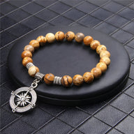 Bracelet homme en pierres naturelles marron avec charm boussole en métal argenté sur support noir.