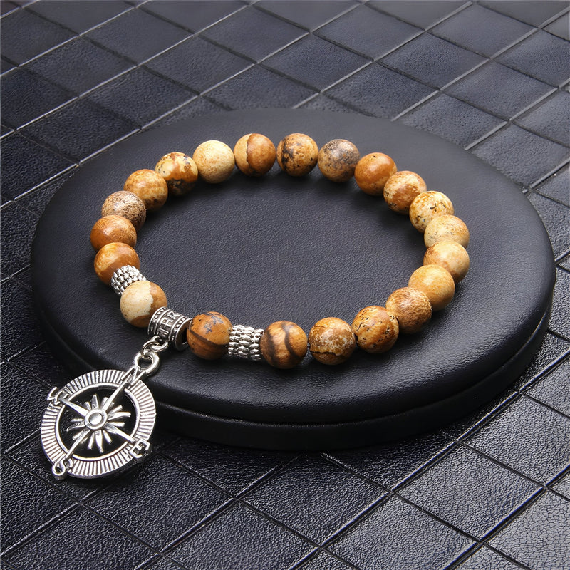 Bracelet homme en pierres naturelles marron avec charm boussole en métal argenté sur support noir.