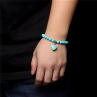 Bracelet mixte en perles turquoise avec pendentif cœur assorti sur poignet.
