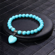 Bracelet mixte en pierres turquoise rondes avec charm cœur turquoise brillant et perles argentées.