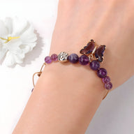 Bracelet en améthyste avec perles rondes et charm papillon violet délicat sur poignet féminin.