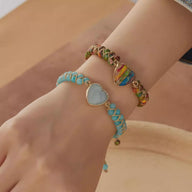 Bracelet turquoise avec motif cœur argenté entrelacé de cordes, porté au poignet avec un bracelet multicolore à motif cœur.