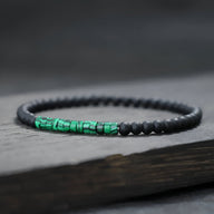 Bracelet fin pour homme en perles noires mates avec accent en pierres malachite vertes éclatantes.