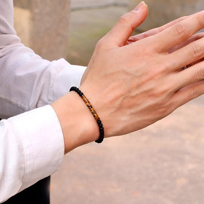 Bracelet fin en pierres d’œil de tigre et obsidienne noires sur poignet d'homme en chemise blanche.