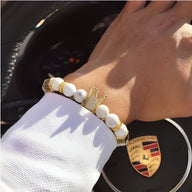 Bracelet homme perles turquoise blanche avec détail couronne dorée sur poignet.