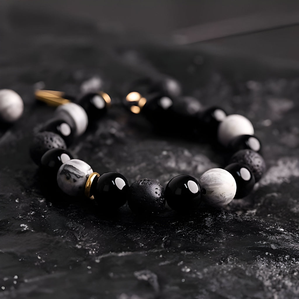 Bracelet homme en pierres noires volcaniques et blanches avec détails dorés sur fond noir texturé.