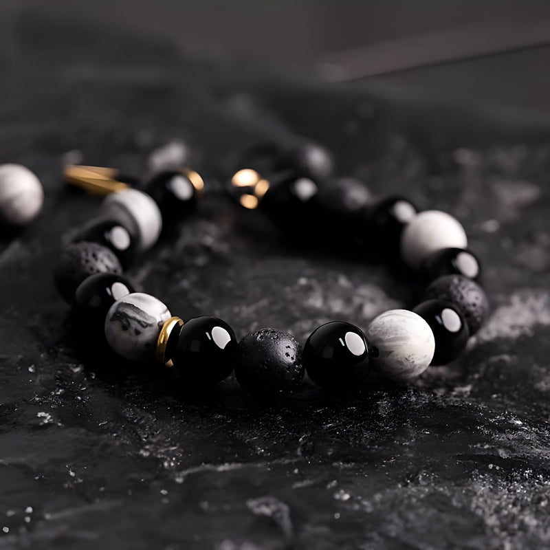 Bracelet homme en pierres noires volcaniques et blanches avec détails dorés sur fond noir texturé.
