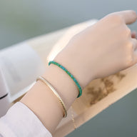 Bracelet fin en pierres turquoises vertes avec un autre bracelet doré tressé, porté au poignet féminin.