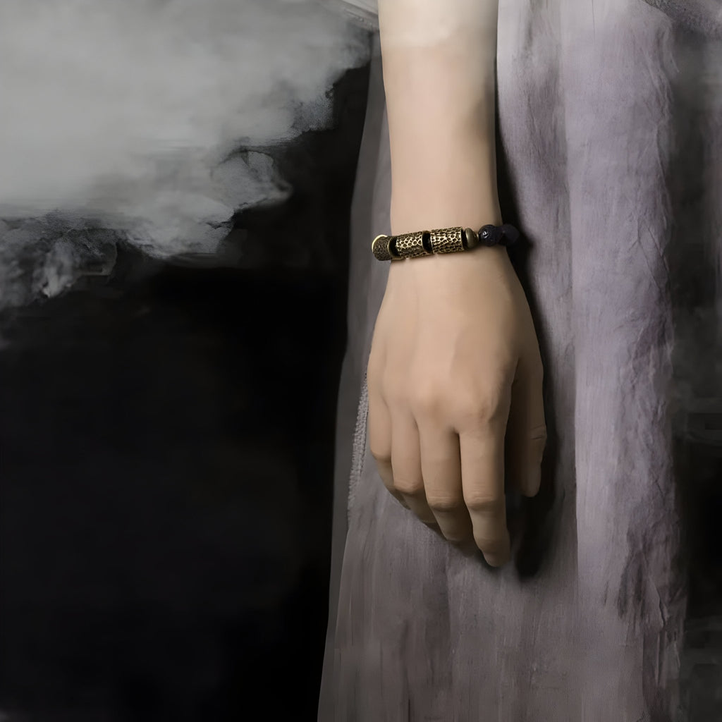 Bracelet femme en pierres volcaniques noires et perles laiton, style ancien, porté au poignet.