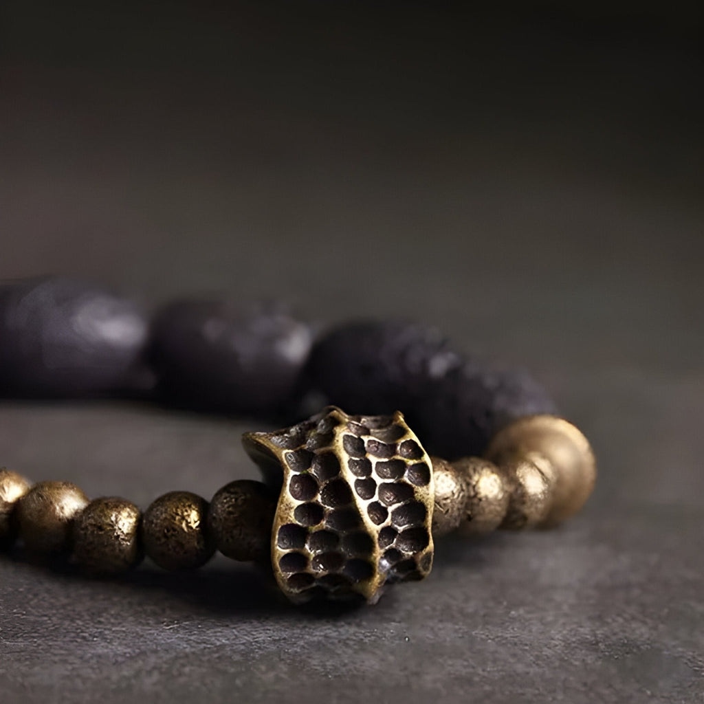 Bracelet femme en pierres volcaniques noires et perles en laiton doré avec pendentif texturé style organique.