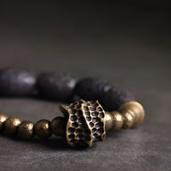 Bracelet femme en pierres volcaniques noires et perles en laiton doré avec pendentif texturé style organique.