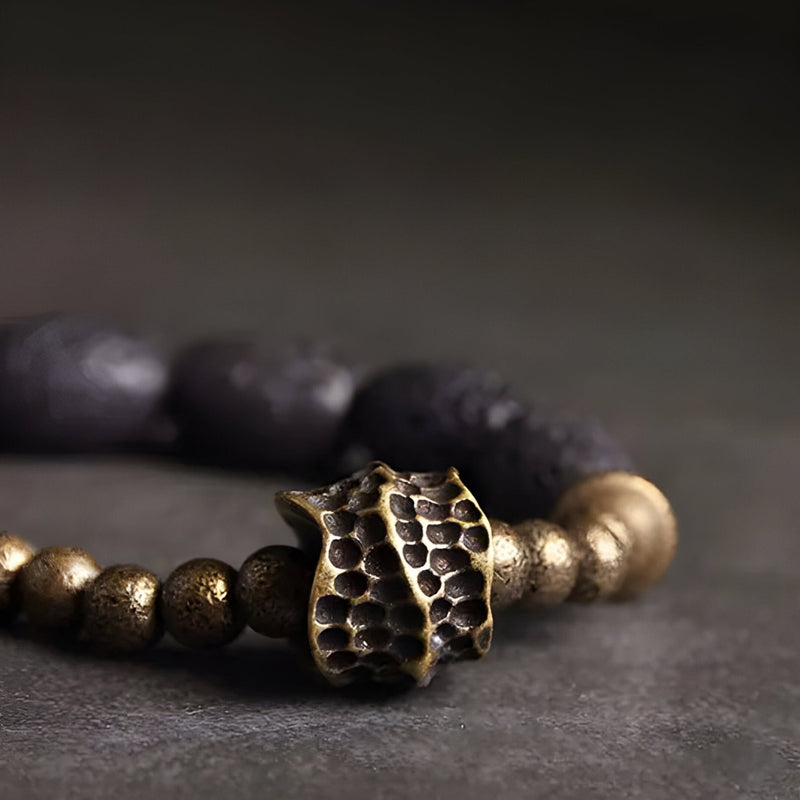 Bracelet femme en pierres volcaniques noires et perles en laiton doré avec pendentif texturé style organique.