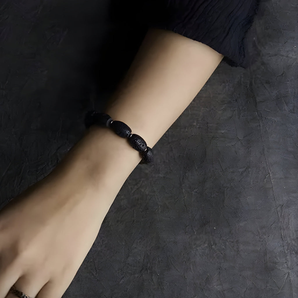 Bracelet femme en pierres volcaniques noires ovales et perles de laiton doré sur poignet.