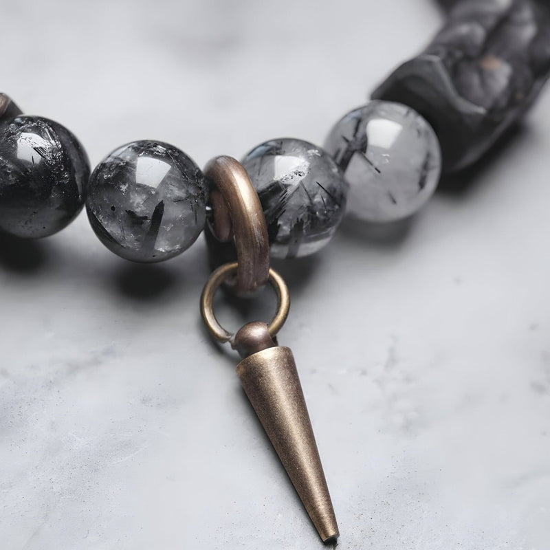 Bracelet mixte en quartz noir et bois d'ébène avec pendentif conique en cuivre vieilli sur fond marbré blanc.