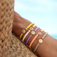 Bracelets en résine colorés avec ornements marguerite et perles sur poignet féminin, tons jaune, violet, rose, orange, beige.