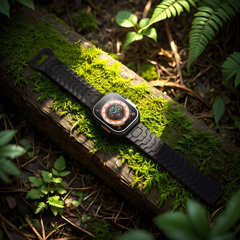 Bracelet en silicone noir à aspect technique pour Apple Watch, résistant et ajustable, fond de nature verte.