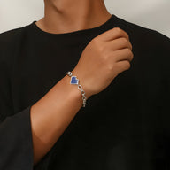 Bracelet en titane argenté avec pendentif cœur bleu porté au poignet d’un homme.