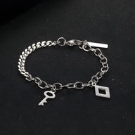 Bracelet en titane argenté à double maille avec breloques clé et losange, fermoir mousqueton.