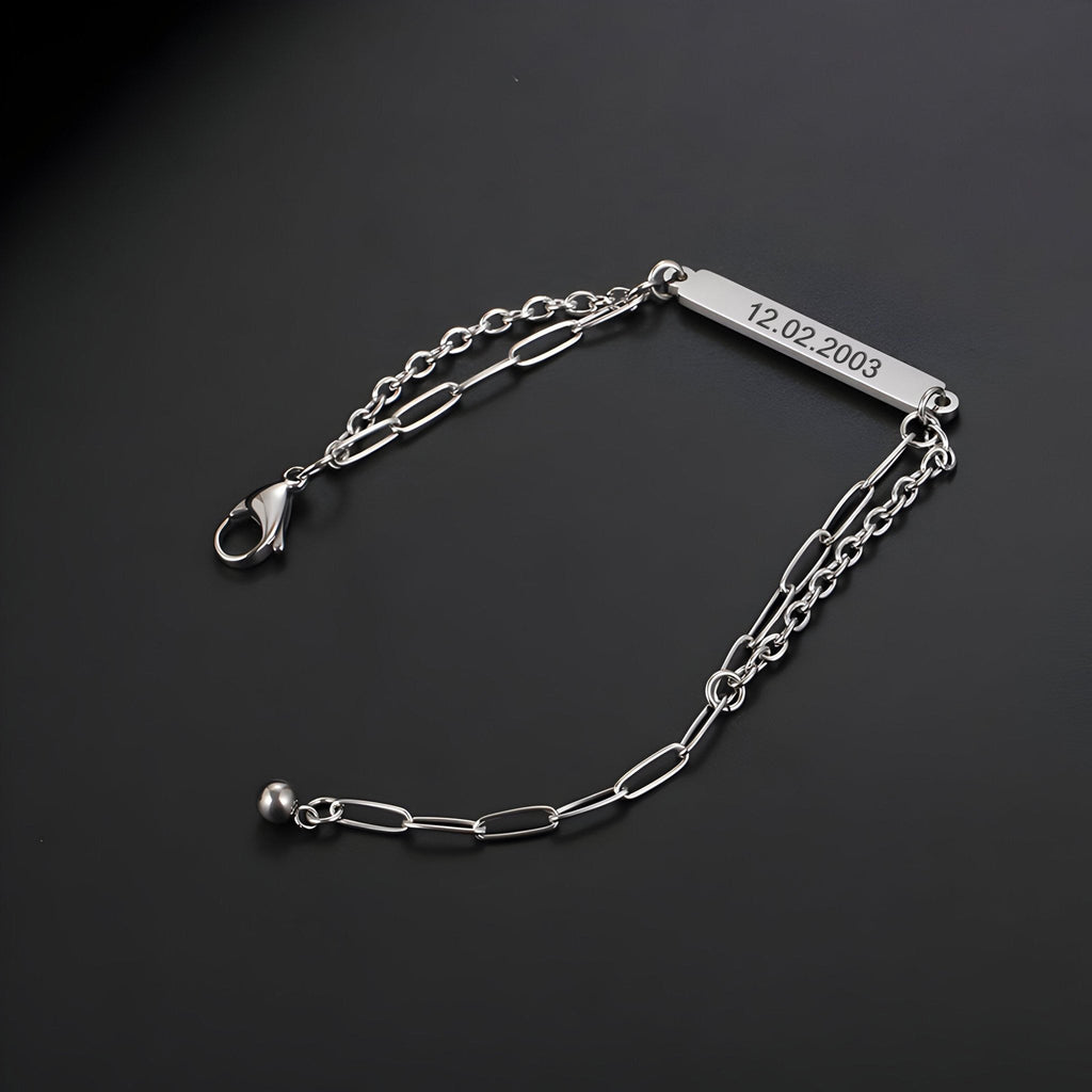 Bracelet gourmette en titane argenté, maille forçat allongée, plaque gravée 12-02-2003, fermoir mousqueton.