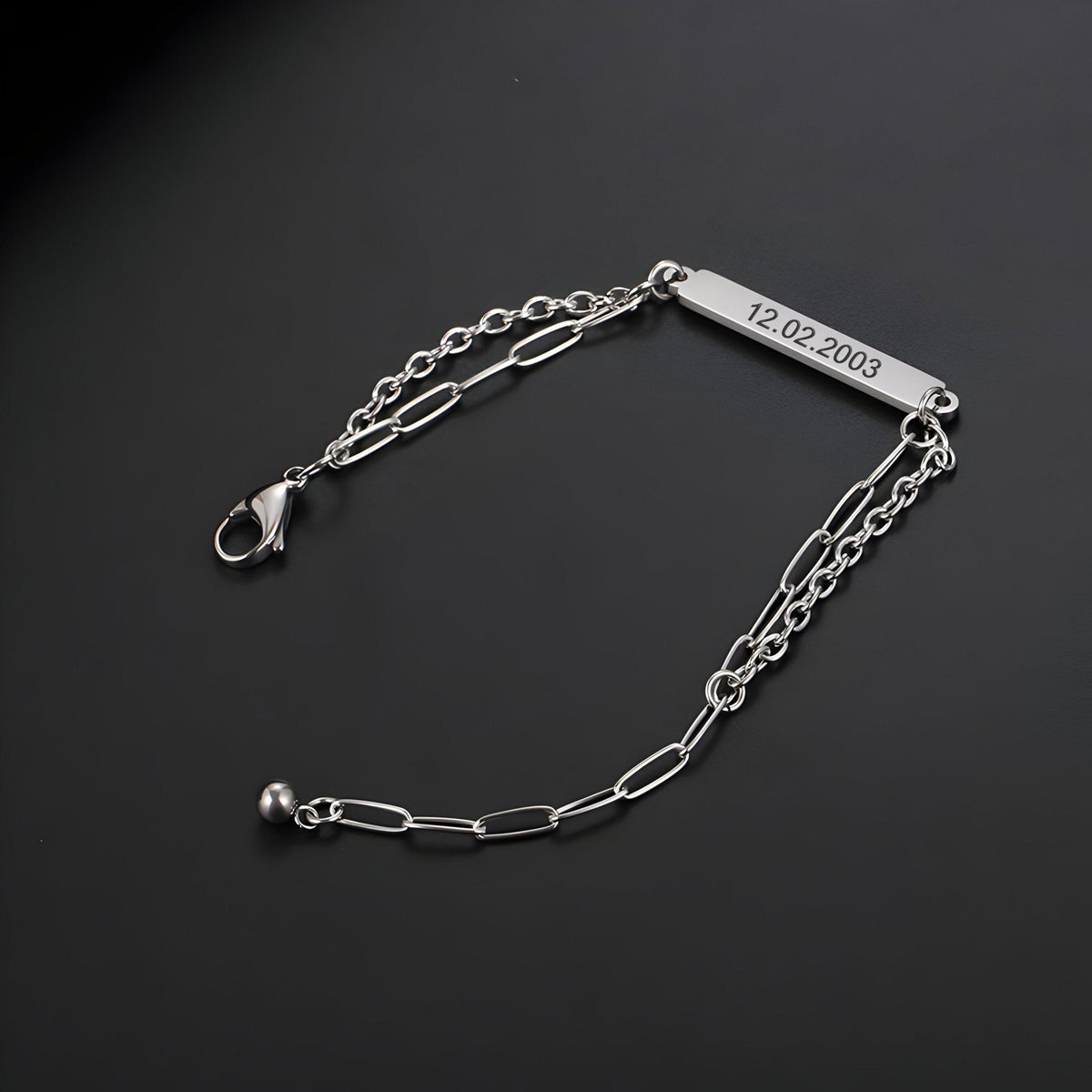 Bracelet gourmette en titane argenté, maille forçat allongée, plaque gravée 12-02-2003, fermoir mousqueton.