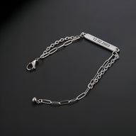 Bracelet gourmette en titane argenté, maille forçat allongée, plaque gravée 12-02-2003, fermoir mousqueton.