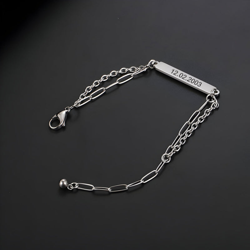 Bracelet gourmette en titane argenté, maille forçat allongée, plaque gravée 12-02-2003, fermoir mousqueton.