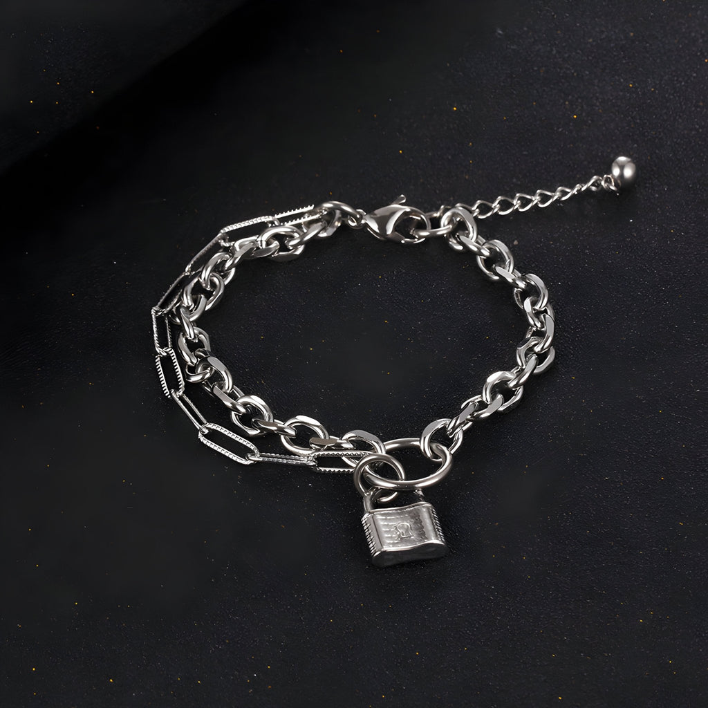 Bracelet mixte en titane argenté à maille forçat avec charm cadenas plaqué argent sur fond noir.