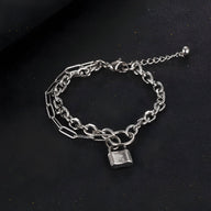 Bracelet mixte en titane argenté à maille forçat avec charm cadenas plaqué argent sur fond noir.