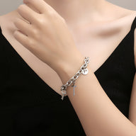 Bracelet en titane argenté à maille forçat avec charms variés, porté au poignet.