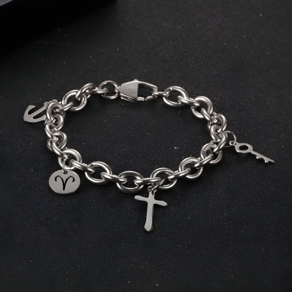 Bracelet en titane argenté à maille forçat avec trois charms, dont une croix, un signe astrologique et une clé.