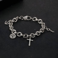 Bracelet en titane argenté à maille forçat avec trois charms, dont une croix, un signe astrologique et une clé.