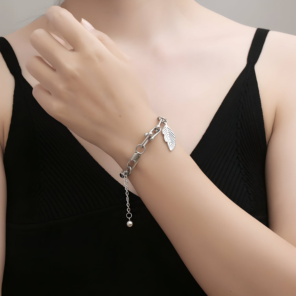 Bracelet en titane argent avec maille spiga et charm plume délicate porté au poignet féminin.