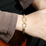 Bracelet en titane doré avec motif infini et chaîne maillon sur poignet.