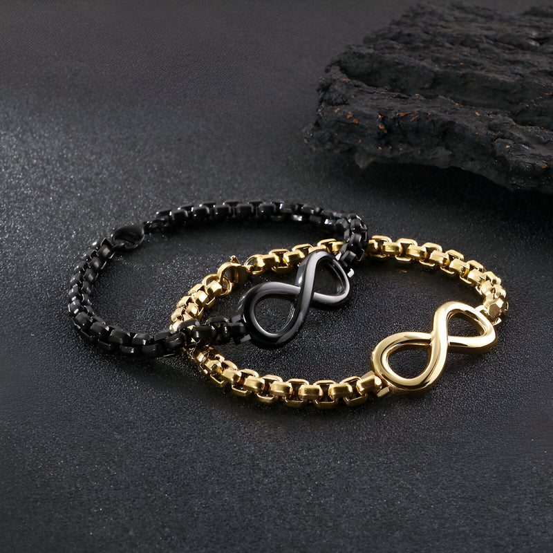 Deux bracelets en titane, un noir et un doré, avec motif infini au centre sur chaîne masculine.