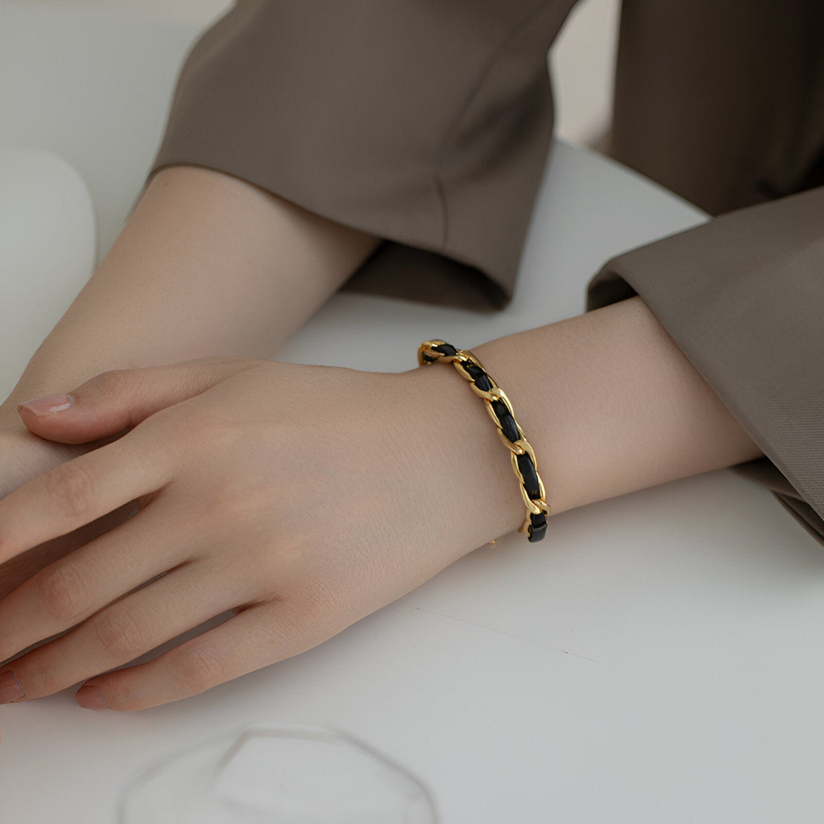 Bracelet en titane plaqué or avec cordelette en cuir noir, style Constance, porté au poignet.
