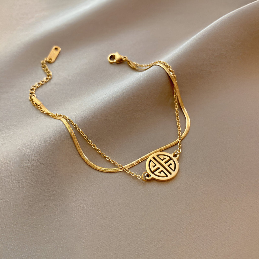 Bracelet en titane plaqué or 18 carats avec médaillon rond à motif géométrique, chaîne fine et fermoir mousqueton.