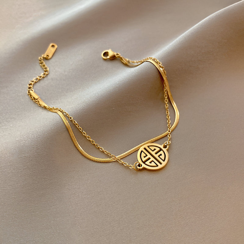 Bracelet en titane plaqué or 18 carats avec médaillon rond à motif géométrique, chaîne fine et fermoir mousqueton.