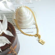 Bracelet fin en titane plaqué or 18 carats avec perles naturelles et pendentif rectangle gravé.