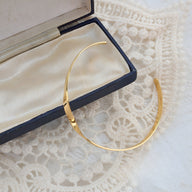 Bracelet rigide en titane plaqué or 18 carats au design distorsion élégant dans un écrin noir et beige.