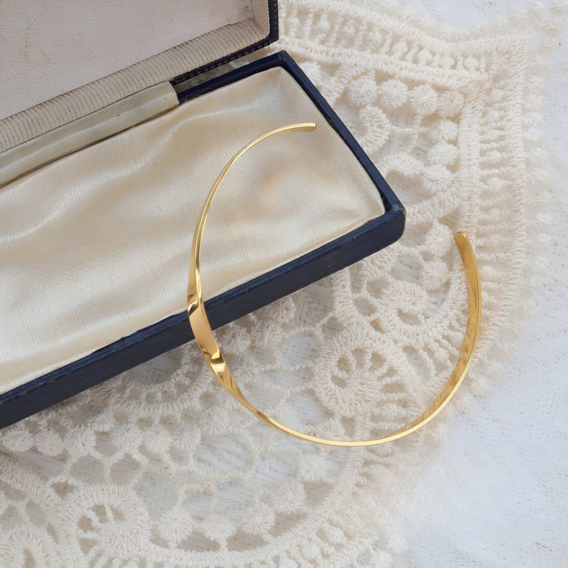 Bracelet rigide en titane plaqué or 18 carats au design distorsion élégant dans un écrin noir et beige.