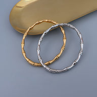 Bracelet bambou en titane plaqué or 18 carats couleur or et argent brillant sur fond gris.