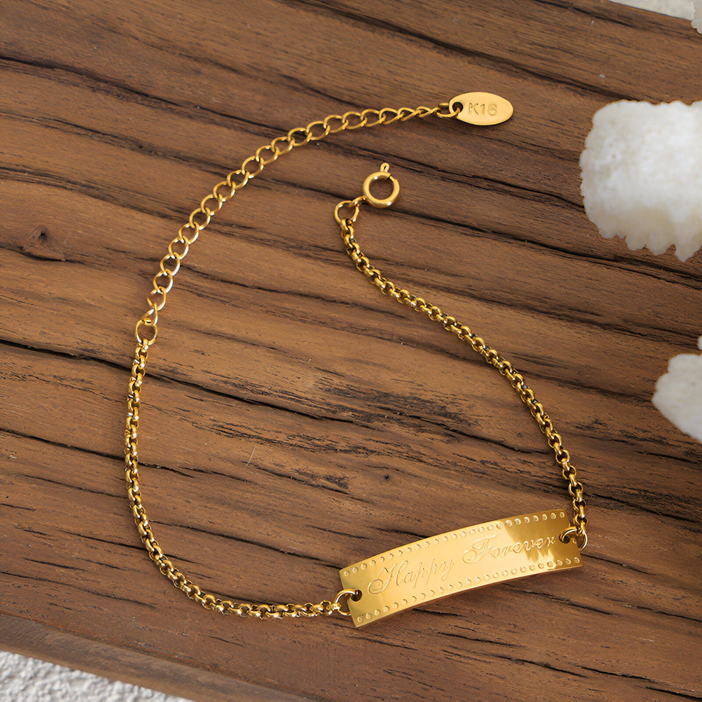 Bracelet fin en titane plaqué or 18 carats avec plaque gravée "Happy Forever" sur chaîne délicate.