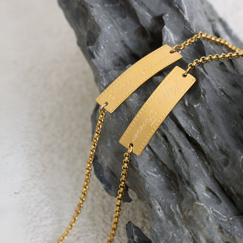 Bracelet fin en titane plaqué or 18 carats avec plaques rectangulaires gravées sur chaîne délicate.