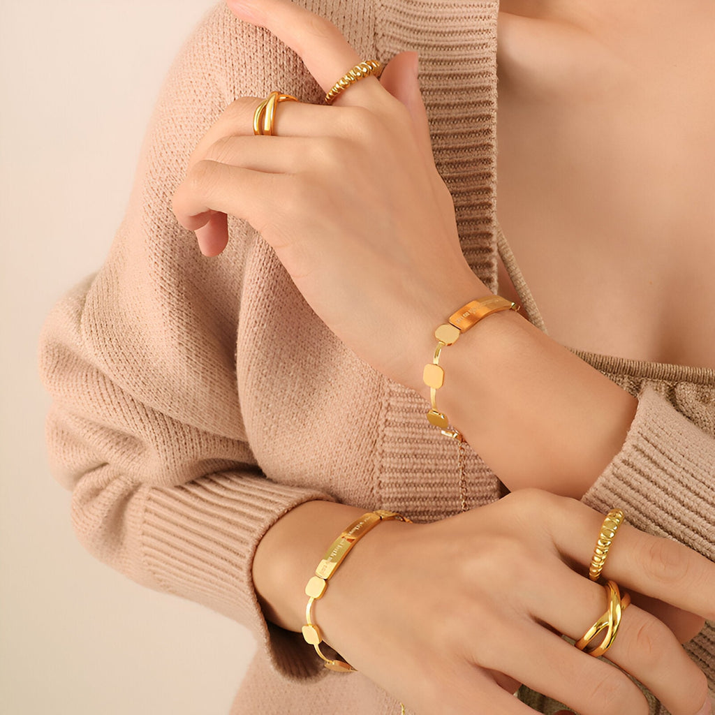 Bracelet en titane plaqué or 18 carats avec maillons carrés et finition brillante, porté avec bagues assorties.