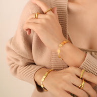 Bracelet en titane plaqué or 18 carats avec maillons carrés et finition brillante, porté avec bagues assorties.