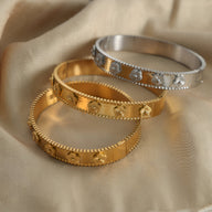 Bracelets jonc en titane plaqué or et argent avec motifs fleurs en relief et bords festonnés.