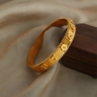 Bracelet jonc en titane plaqué or avec motifs floraux en relief et détails de perles fines.